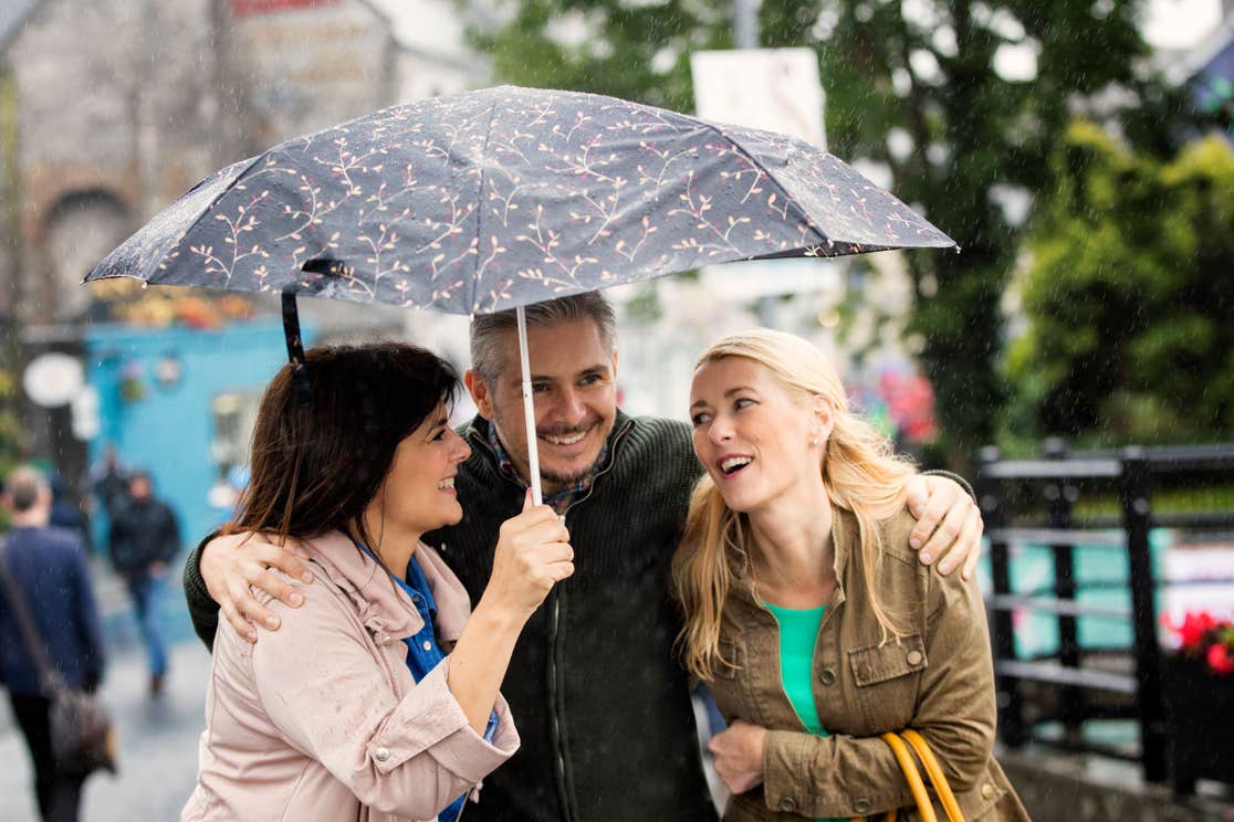 Three people standing under an umbrella in Ennis in County Clare