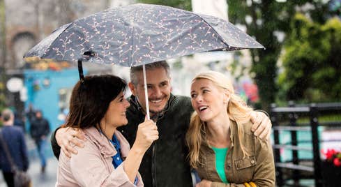 Three people standing under an umbrella in Ennis in County Clare