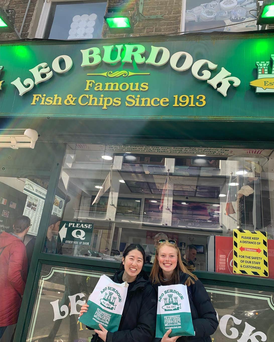 Two women standing outside Leo Burdocks fish and chip shop.