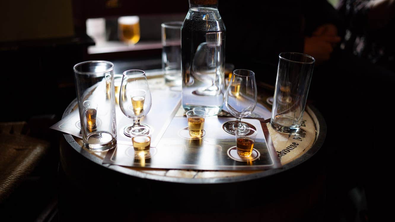 A bottle of whiskey and glasses sitting on a wooden whiskey barrel acting as a table