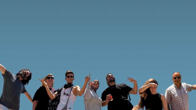 Looking up at a line of 7 happy people, some waving their arms, against a clear blue sky.