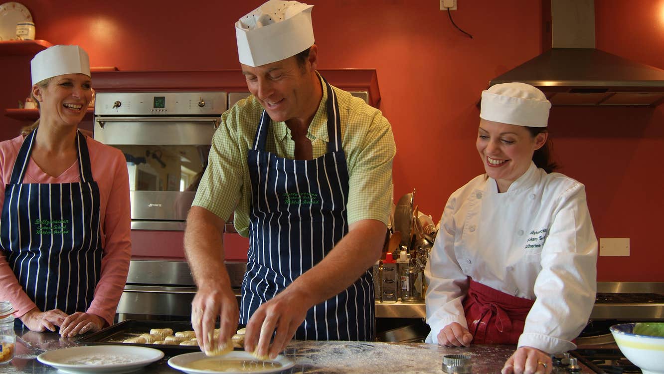 A chef showing two students how to cook in a red kitchen in Ballyknocken, County Wicklow