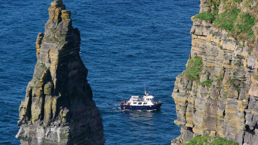 A boat on the water besides towering sea cliffs