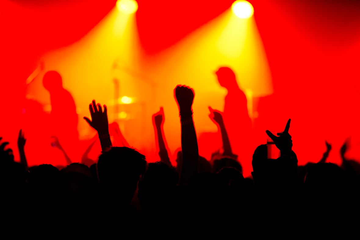 Orange lights on musicians on a stage with the silhouette of a crowd.