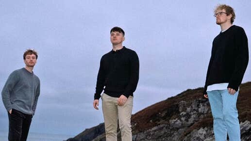 3 men standing apart outdoors with dull sky