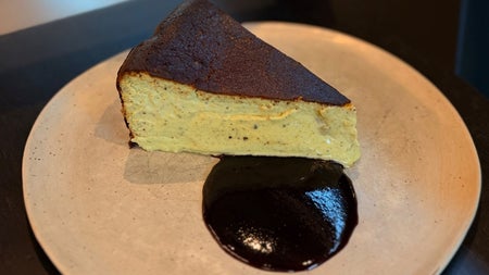 A slice of baked cheesecake on a ceramic plate with a dark chocolate sauce