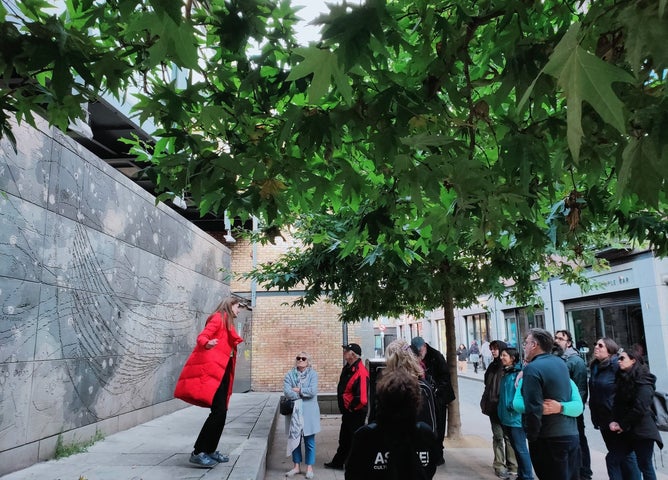 A tour guide speaking to a group of people at an ornate wall on a city street