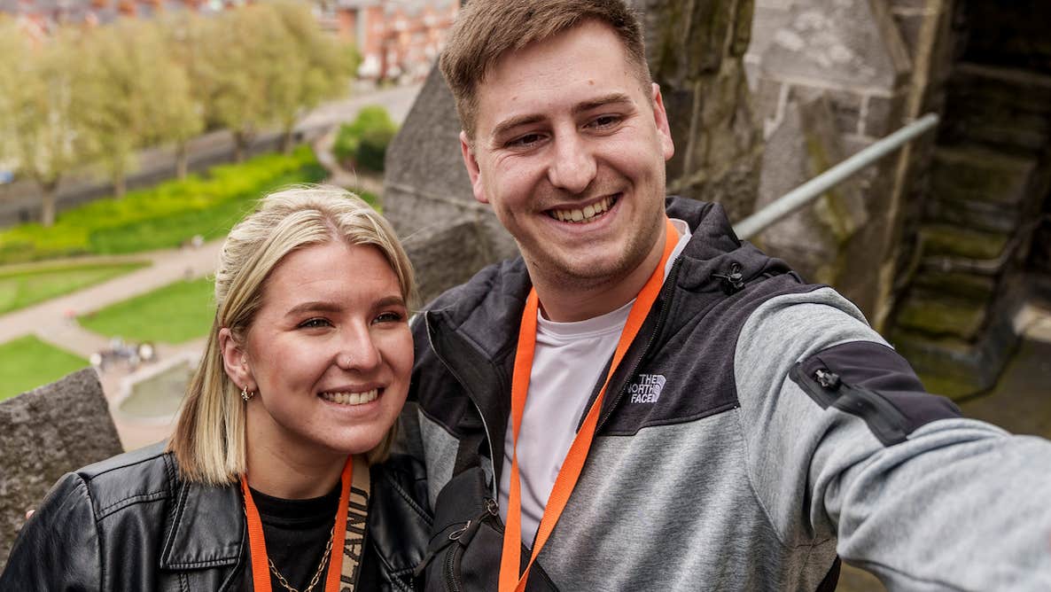 First Fortnight in partnership with St Patrick's Cathedral, 2 smiling people taking a selfie up high in stone building with blurry view of city below