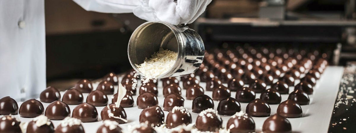 A row of chocolate sweets being sprinkled with flakes during manufacturing