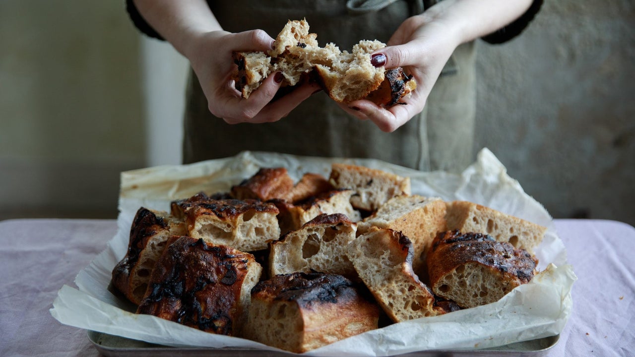 Hands tearing fresh baked bread from a tray on a table with a white tablecloth