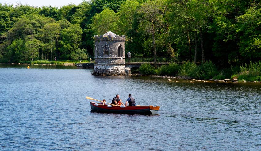 A small wooden row boat passing a castle on Lough Key.