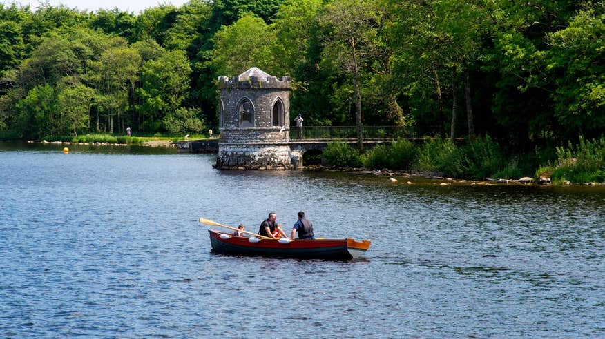 A small wooden row boat passing a castle on Lough Key.