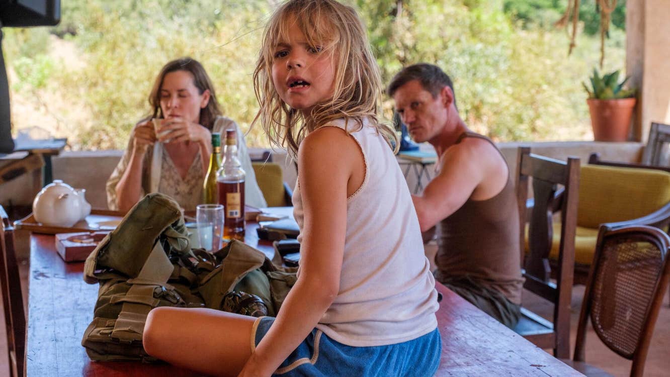 A little girl is sitting on a dining table. A man and a woman are sitting at it.