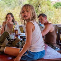 A little girl is sitting on a dining table. A man and a woman are sitting at it.