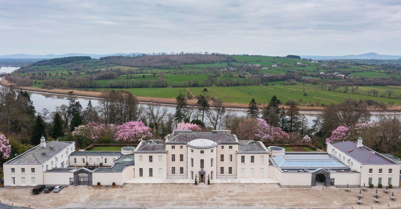 An aerial view of a large period mansion house with colourful trees in the background