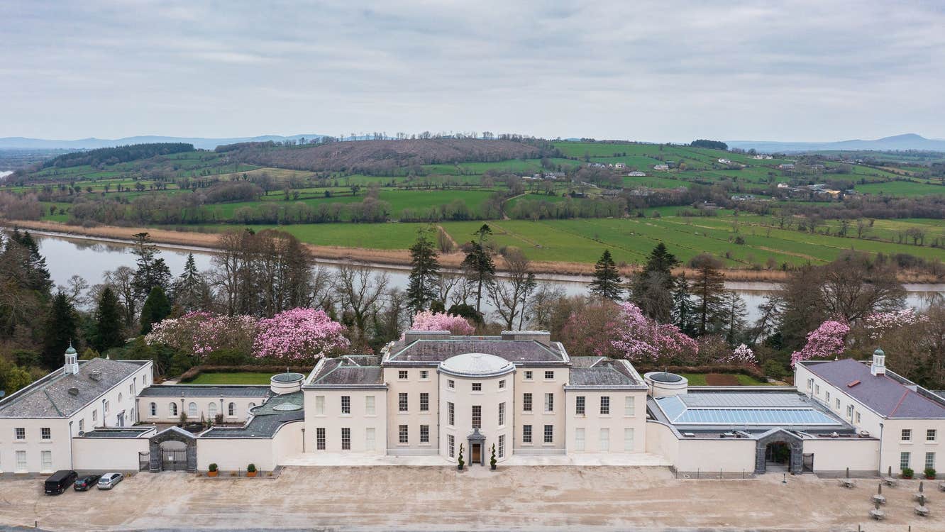 An aerial view of a large period mansion house with colourful trees in the background