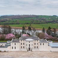 An aerial view of a large period mansion house with colourful trees in the background
