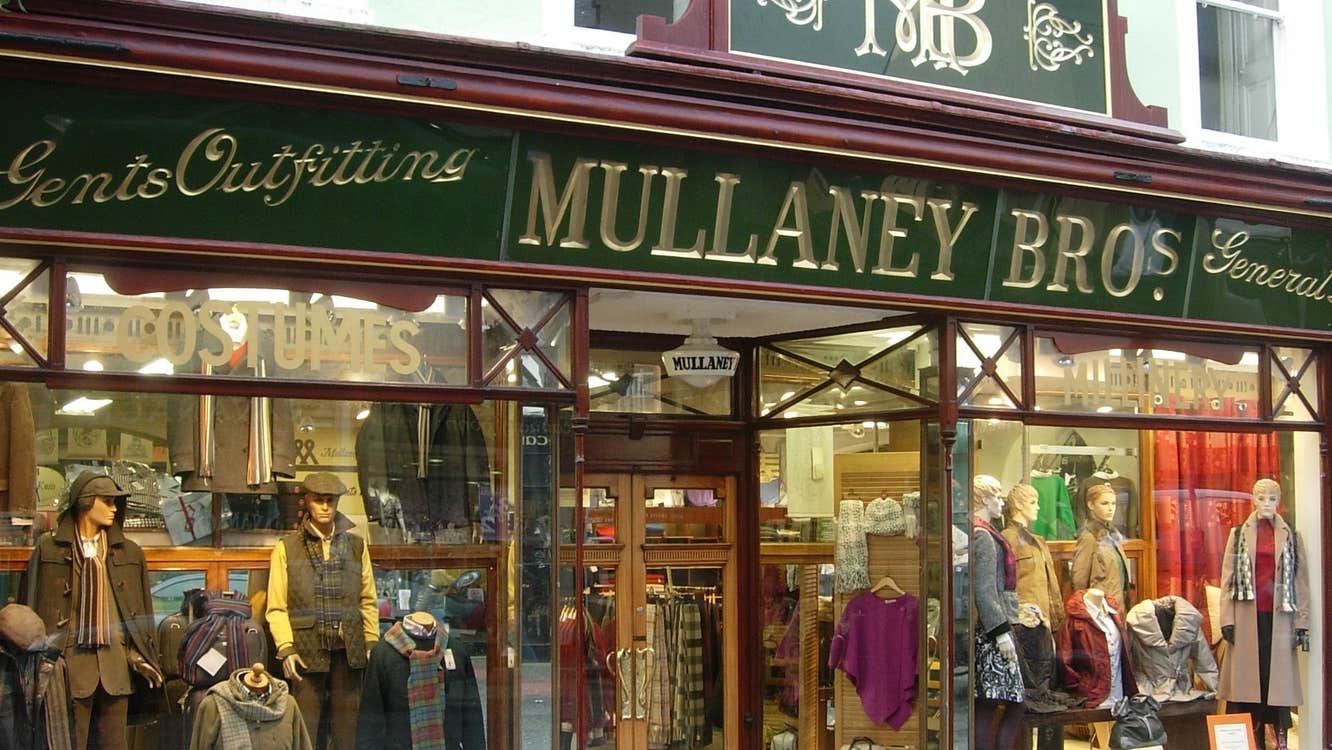 Shop front with windows displaying mannequins and clothes with mullaney bros written in gold against a green background above the entrance