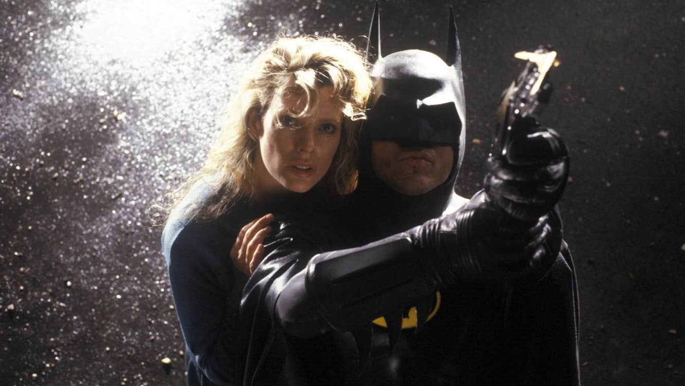 Batman is pointing a grapple-gun. A blonde woman is behind him.
