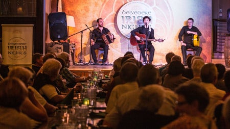 Three traditional musicians perform on a stage in front of an audience