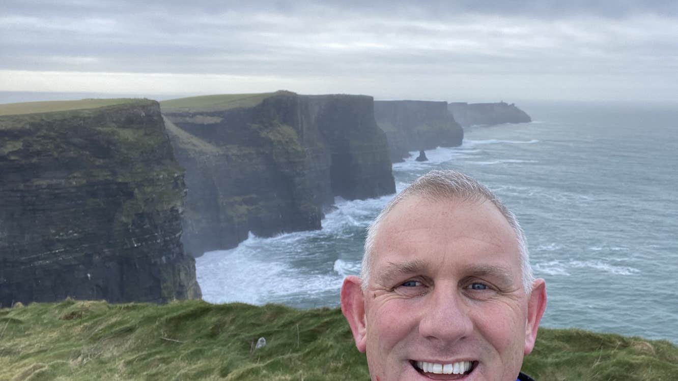 Selfie of a man in a blue jacket with cliffs and the sea in the background