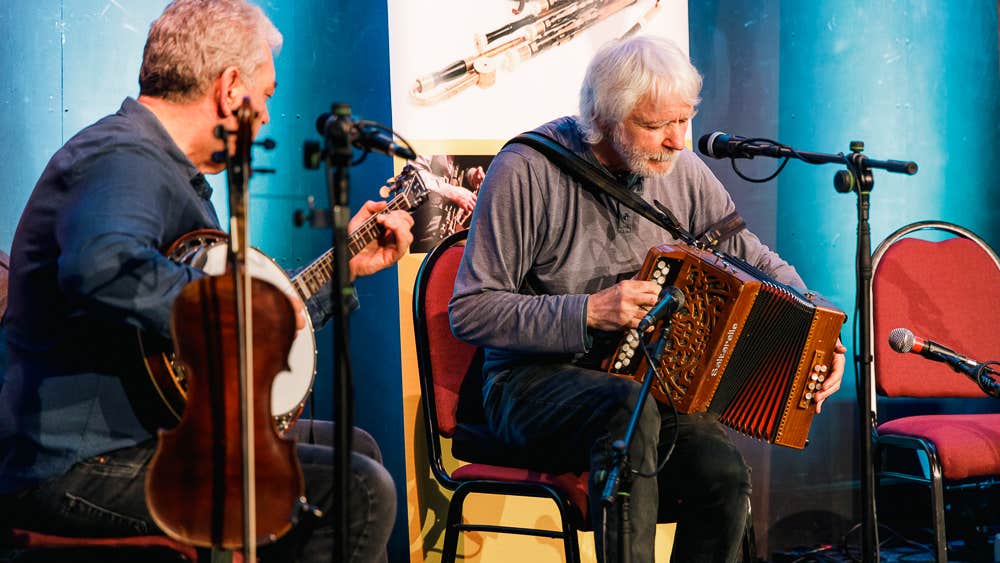 2 seated musicians playing on a small stage.