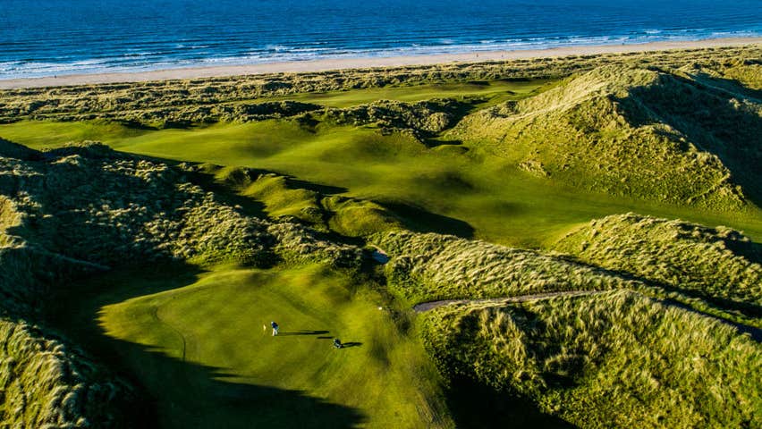 Aerial shot of a golfer on a hilly golf green with the sea in the background
