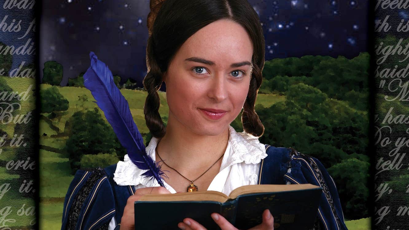 A woman in costume is smiling, holding an open book with a feather quill in her left hand.