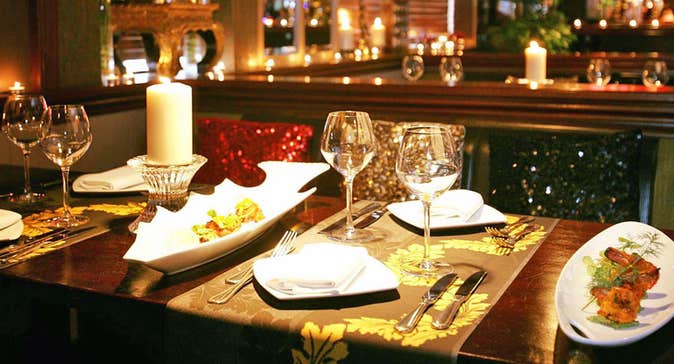 A table set for four in an Indian restaurant with a lit candle on the table and starter dishes to the side