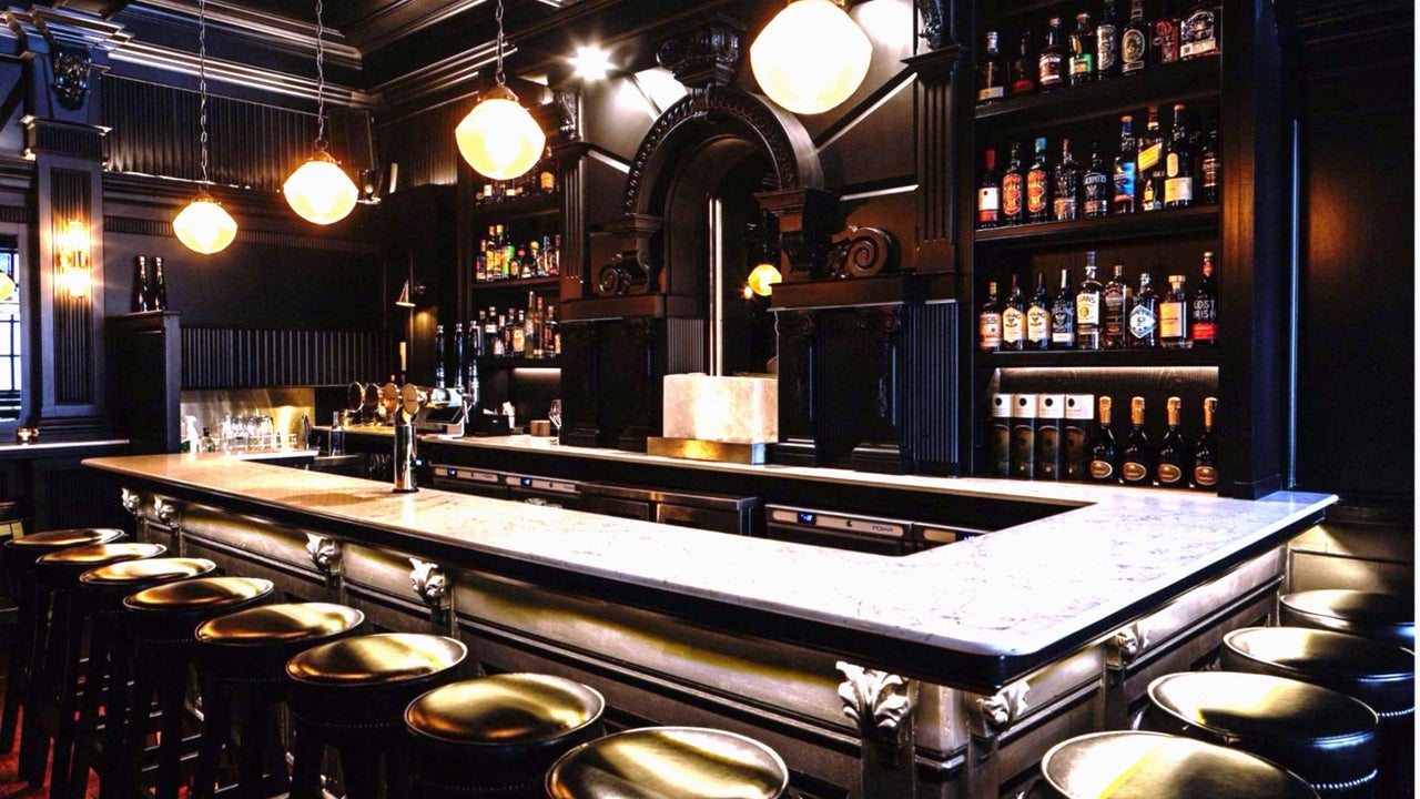 A rectangular cocktail bar surrounded by empty bar stools in a low light environment