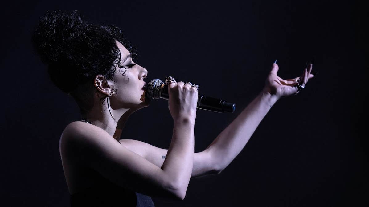 Noami Banks, vocalist - side view of woman singing into hand held mic with arm outstretched