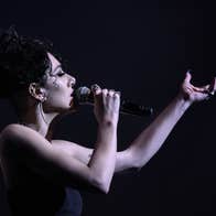 Noami Banks, vocalist - side view of woman singing into hand held mic with arm outstretched