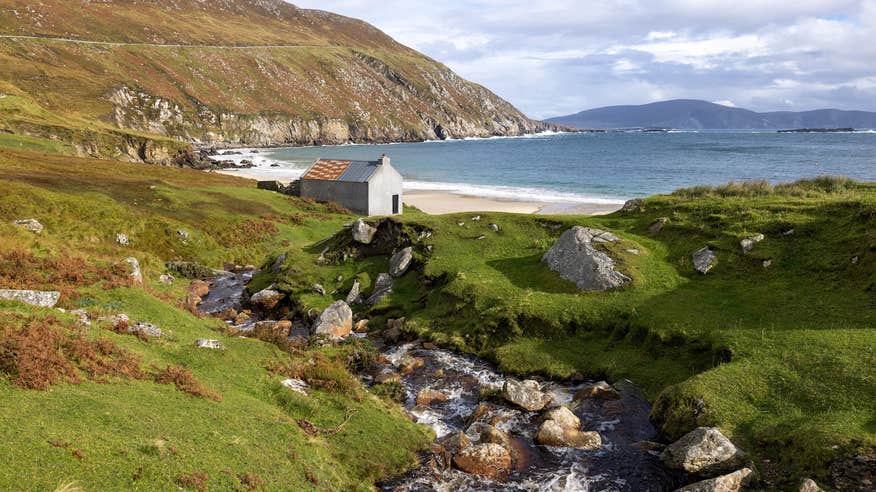 Scenic shot of Keem Bay in Achill, featuring a small cottage facing the beach. 
