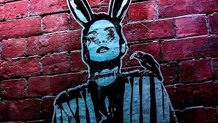Black and blue painted image of person with rabbits ears on red brick wall
