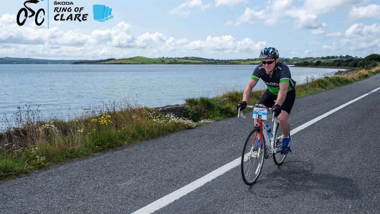 A cyclist of a road along side a way body of open water with hills in the distance.