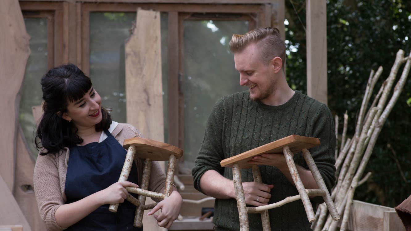 Two people holding wooden stools and smiling