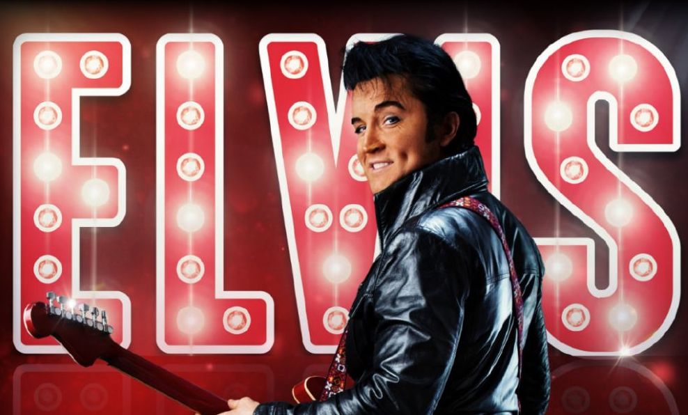 A man in leather jacket holding a guitar is looking back over his shoulder smiling with large red lit up letters behind.