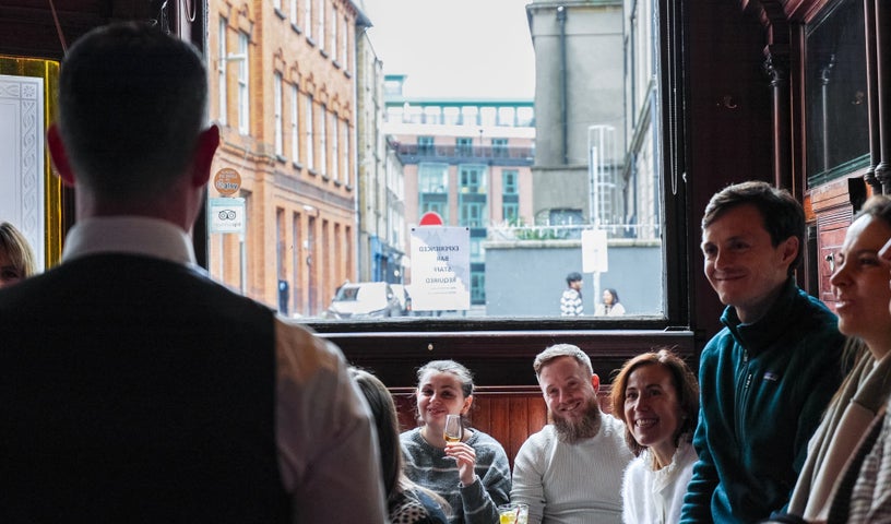 A man with his back to the camera taking to a group of people in a bar