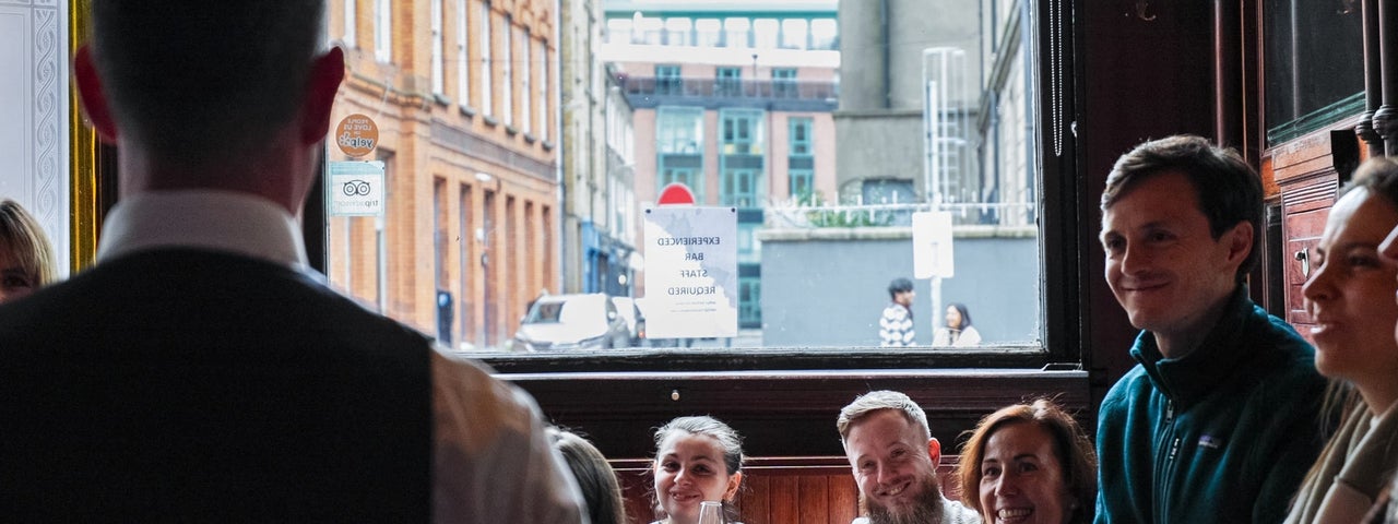 A man with his back to the camera taking to a group of people in a bar