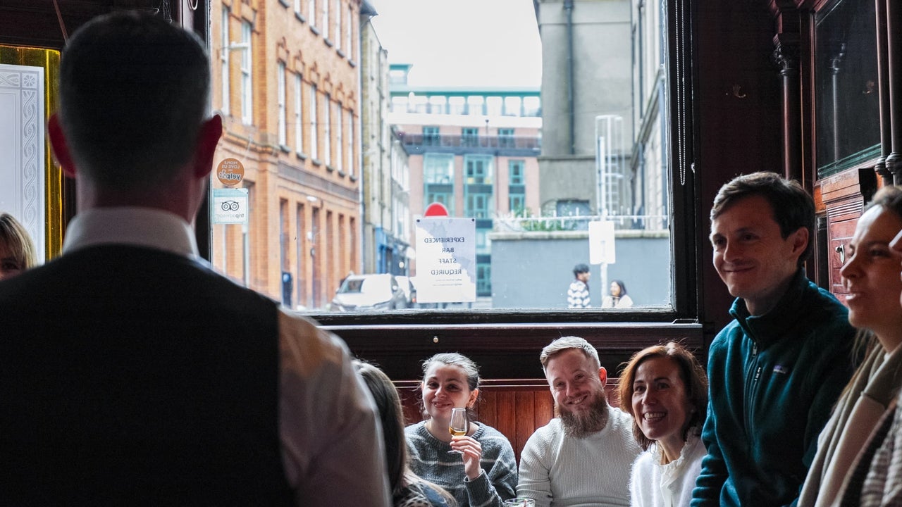 A man with his back to the camera taking to a group of people in a bar