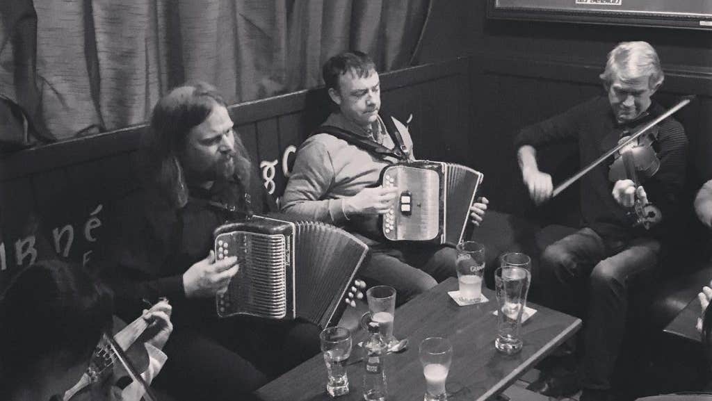 Fleadh na Bealtaine 2026 Galway - people seated playing musical instruments with table holding drinks.