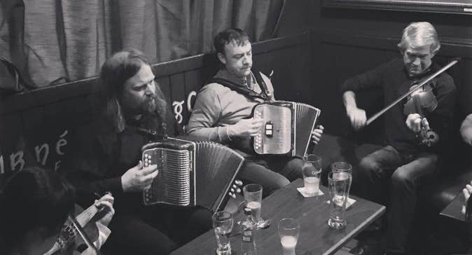 Fleadh na Bealtaine 2026 Galway - people seated playing musical instruments with table holding drinks.