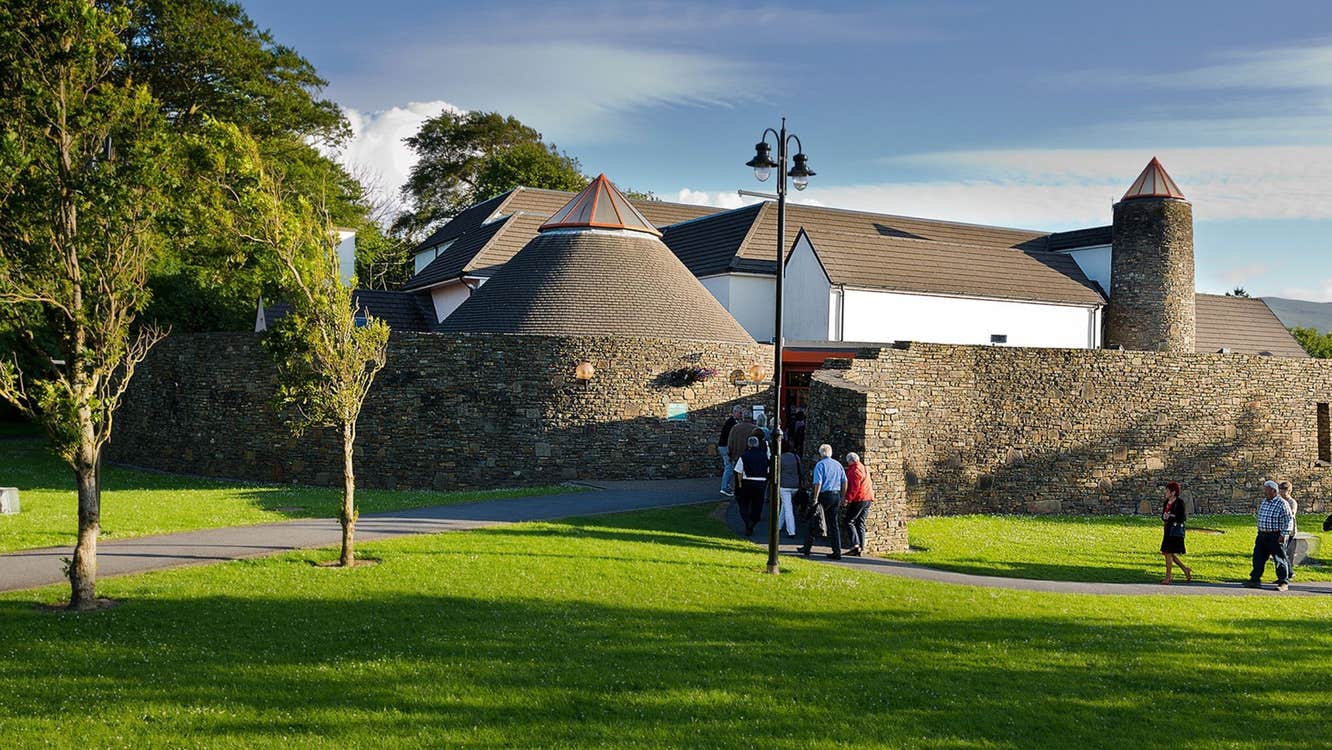 People walking through a park with trees into a building with a round stone wall