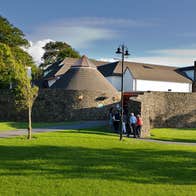 People walking through a park with trees into a building with a round stone wall