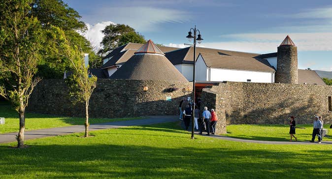 People walking through a park with trees into a building with a round stone wall