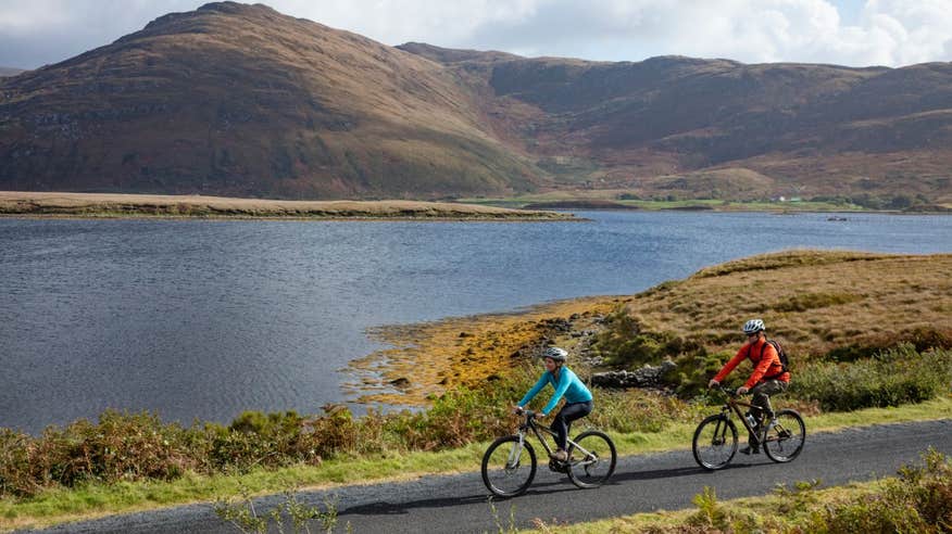 Two people cycling along the Great Western Greenway with sea and mountain views