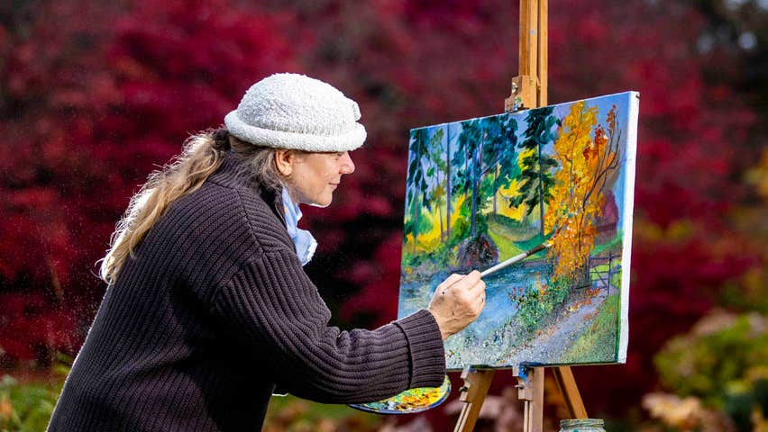 An artist outdoors at her easel painting a landscape