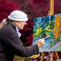 An artist outdoors at her easel painting a landscape