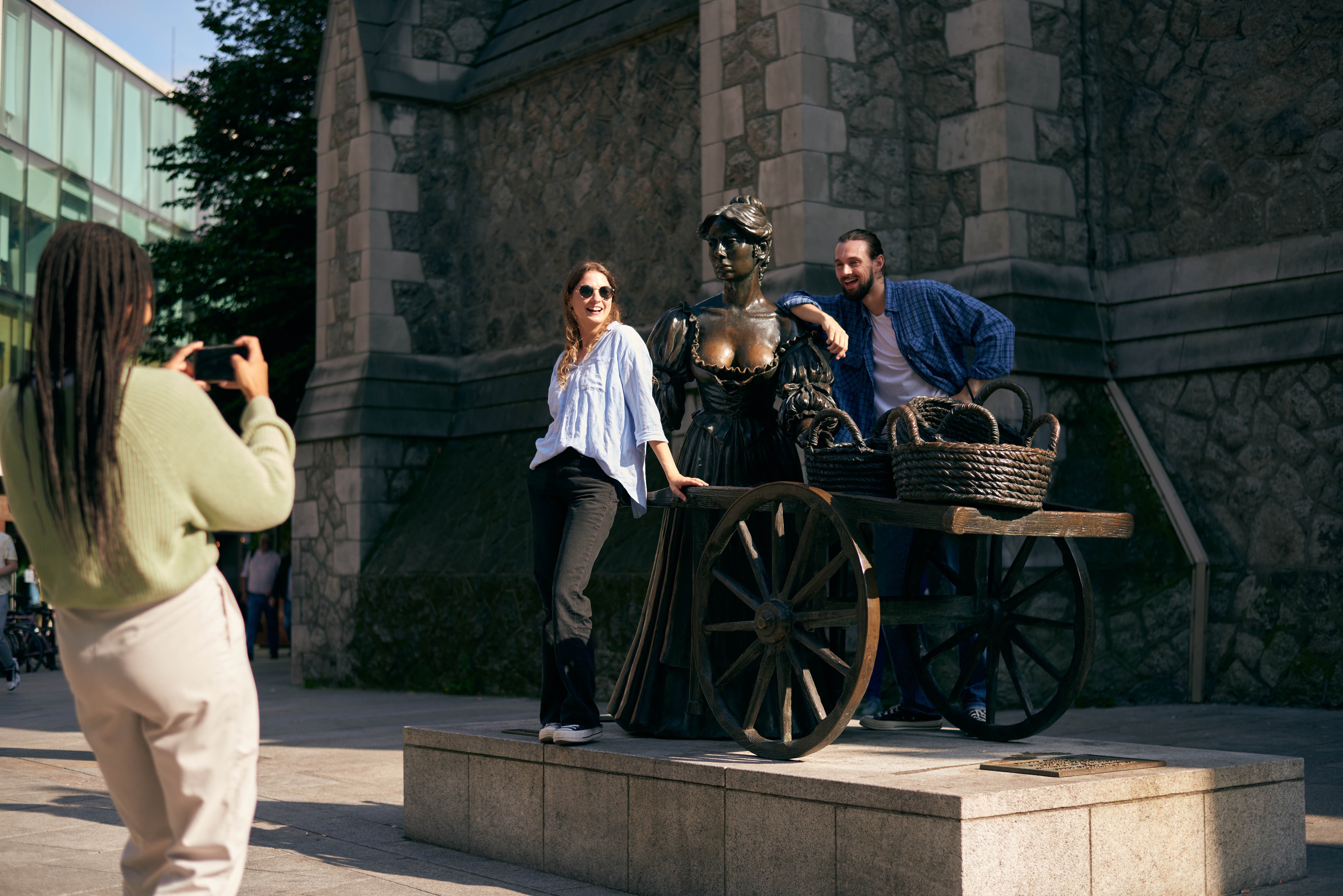 A group of friends posing with the Molly Malone statue while another friend takes their picture.