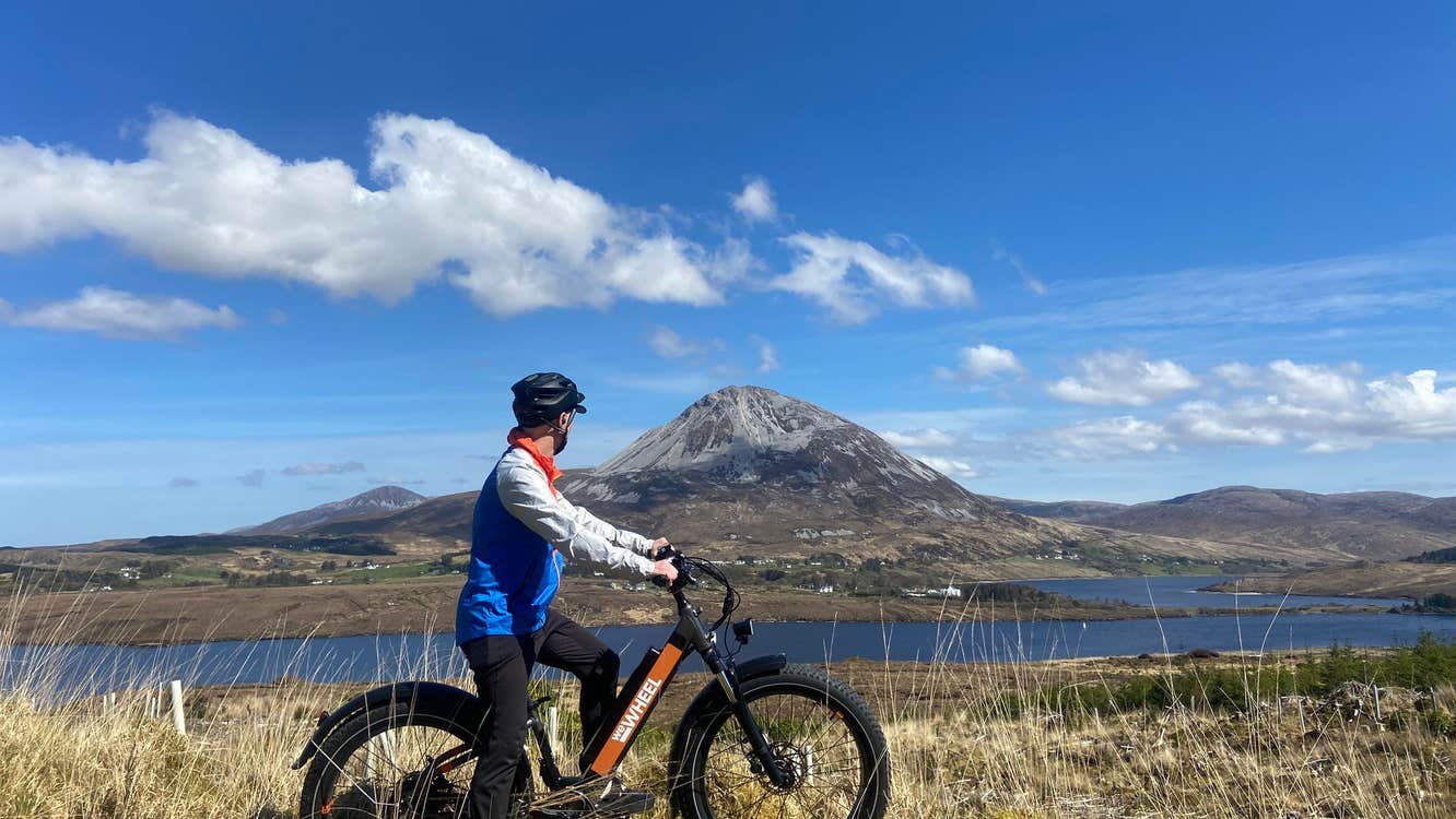 Person wearing a helmet on a bike next to a lake in front of a mountain